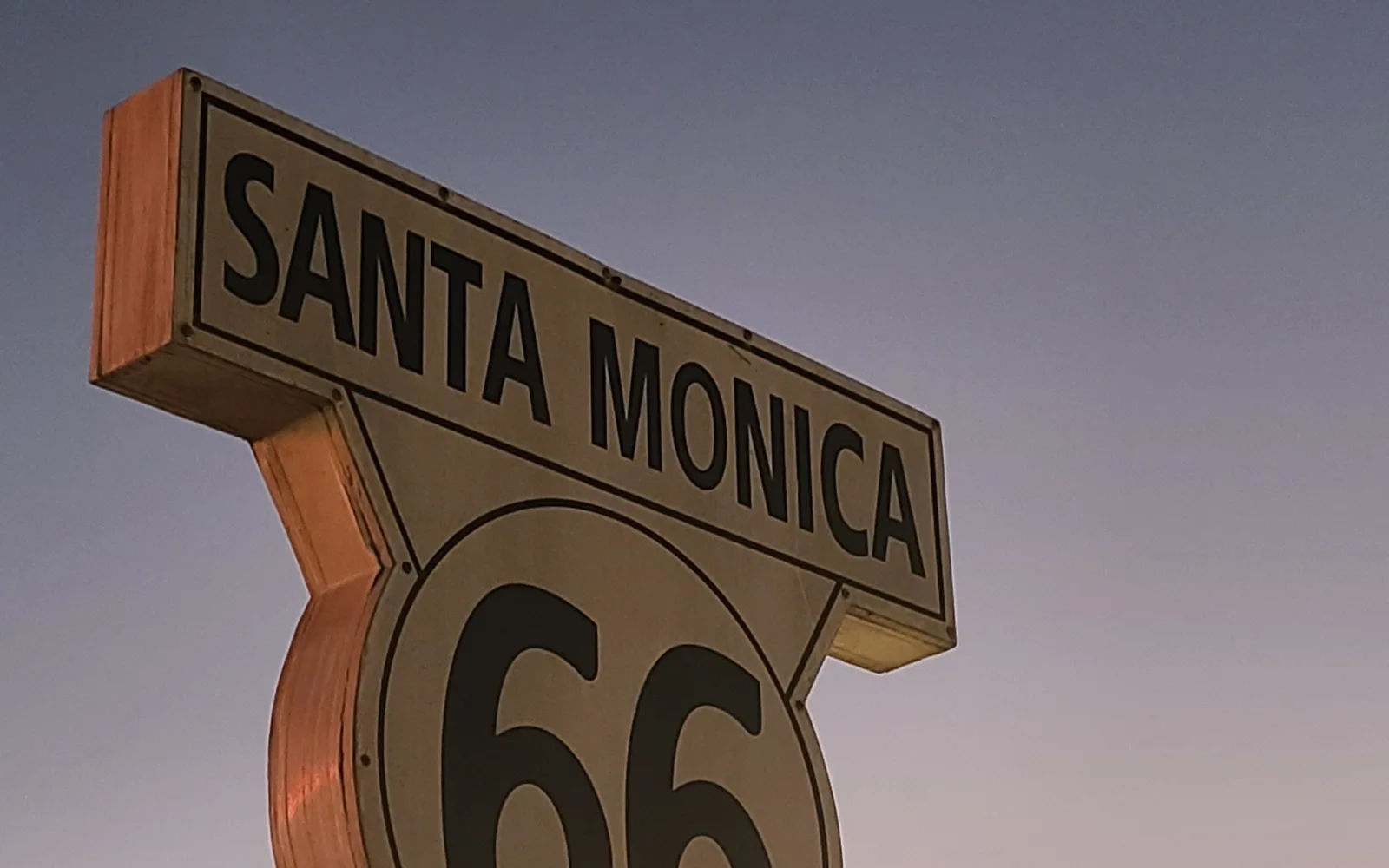 Sunset at the Santa Monica beach terminus of Historic Route 66, with the Pacific Ocean and sky in warm golden tones